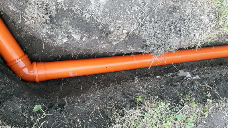 Image of a new orange PVC sewer pipe installed in the ground during house renovation after availing line locating service.